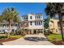 Charming raised beach home featuring palm trees, covered parking, and a classic coastal design at 527 Bay Drive Ext., Garden City Beach, SC 29576