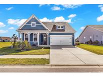 Charming blue home with a two-car garage, landscaped yard, and inviting front porch on a sunny day at 684 Wailea Circle, Little River, SC 29566