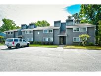 View of building exterior with gray wood siding, windows, roof access, landscaping, and asphalt parking lot at 10301 N Kings Hwy. # 21-5, Myrtle Beach, SC 29572