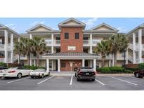 Attractive condo building featuring palm trees, a brick facade, and covered balconies with white railings at 1000 Ray Costin Way # 107, Garden City Beach, SC 29576