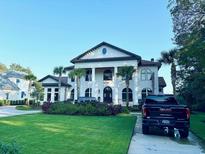 Elegant two-story home featuring a manicured lawn, palm trees, and a classic architectural design with prominent columns at 4110 Gray Heron Dr., North Myrtle Beach, SC 29582