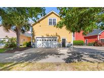Yellow home featuring a two-car garage with a white door and driveway, framed by mature trees at 1516 James Island Ave., North Myrtle Beach, SC 29582