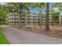 View of the condo complex surrounded by trees, landscaping, and a walking path with a bench at 415 Ocean Creek Dr. # 2245, Myrtle Beach, SC 29572