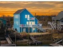 Charming blue two-story waterfront home with multiple balconies and private dock access, perfect for coastal living at 154 Sand Dollar St., Holden Beach, NC 28462