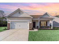 Inviting single-story home featuring a two-car garage, manicured lawn, and charming front porch under a colorful sunset at 610 Lightwood Dr., Conway, SC 29526