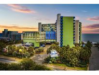 An exterior view of the Coral Beach Resort with a palm-lined entrance, and a sunset in the background at 1105 S Ocean Blvd. # 724, Myrtle Beach, SC 29577