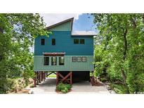 Two-story blue home featuring a unique design with wooden supports and lush green landscaping at 329 Kaufman St., Georgetown, SC 29440