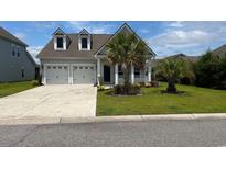 Charming home showcasing a two-car garage, palm trees, and manicured lawn at 692 Cherry Blossom Dr., Murrells Inlet, SC 29576