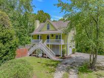 Charming yellow two-story home with a spacious elevated porch and stairway surrounded by mature trees at 1050 Hagley Dr., Pawleys Island, SC 29585