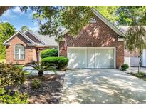 Brick home featuring a two-car garage and a well-manicured front yard with mature trees and plantings at 3071 Alice Ln., Little River, SC 29566