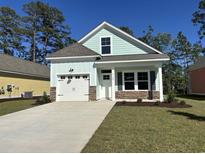 Charming, light blue single-Gathering home featuring a well-manicured lawn and stone accents under a bright blue sky at 3129 Tiger Tail Rd., Conway, SC 29526