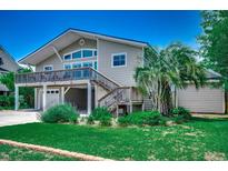 Charming coastal home with a wooden deck, a well-kept lawn and a palm tree on a sunny day at 1924 Pompano Dr., Garden City Beach, SC 29576