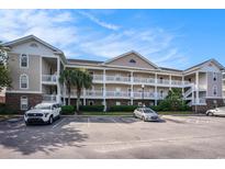 Three-story condo building with a beautiful facade, exterior staircases, and a well-kept parking area under a bright blue sky at 5751 Oyster Catcher Dr. # 315, North Myrtle Beach, SC 29582
