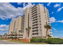 A multi-story condo building featuring private balconies, palm trees, and lush landscaping against a bright sky at 1990 N Waccamaw Dr. # 807, Murrells Inlet, SC 29576