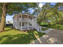 Charming two-story home featuring a spacious porch and staircase surrounded by lush green trees and landscaping at 409 2Nd Ave. S, Myrtle Beach, SC 29577