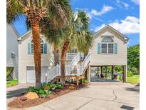 Charming two-story coastal home with mature palms, a garage, and elevated living, offering a glimpse of the waterway at 521 Bay Drive Ext., Garden City Beach, SC 29576