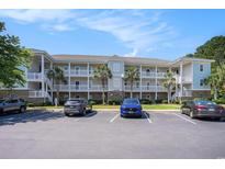 Condo complex with three stories and a parking lot and tropical trees under a blue sky with cars at 6253 Catalina Dr. # 1523, North Myrtle Beach, SC 29582