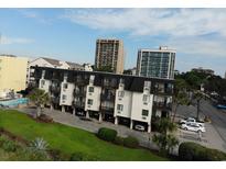 Three-story condo building with black trim, white siding, balconies, covered parking, and beautifully landscaped grounds at 201 76Th Ave. N # E3, Myrtle Beach, SC 29577