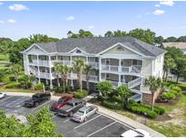 A three-story condo building with white railings, palm trees, and a parking lot in a sunny setting at 5801 Oyster Catcher Dr. # 332, North Myrtle Beach, SC 29582