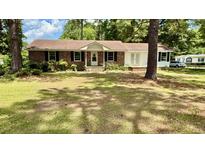 Charming brick home featuring a well-maintained lawn, complemented by mature trees and classic black shutters at 6805 Mclaurin Rd., Mullins, SC 29574