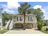Charming raised beach house with a palm tree, covered parking, and inviting staircase leading to the front porch at 914 Dock Pl., Murrells Inlet, SC 29576