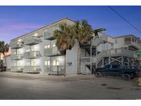 Three-story condominium building featuring stairwells and multiple balconies, surrounded by trees and ample parking spaces at 300 47Th Ave. S # 1F, North Myrtle Beach, SC 29582