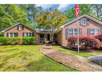 Charming brick home featuring a brick walkway, mature trees, lush landscaping, and a welcoming American flag at 196 John Waites Ct., Georgetown, SC 29440