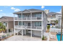 Three-story home featuring double balconies, gray siding, a brick driveway, and a well-manicured landscaped perimeter at 204 33Rd Ave. N, North Myrtle Beach, SC 29582