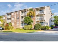 Three-story condo building featuring a brick facade and multiple balconies with white railings and mature landscaping at 1212 Ocean Blvd. S # 202, Surfside Beach, SC 29575