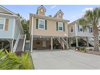 Charming raised beach home with tan siding, green shutters, and covered parking, surrounded by lush landscaping at 4331 Grande Harbour Blvd., Little River, SC 29566