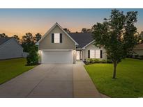 Charming home featuring a two-car garage, manicured lawn, and beautiful landscaping at dusk at 620 Seth Ln., Longs, SC 29568