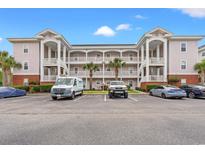 Three story condo building features a parking lot, palm trees, white railings, and light pink paint at 4142 Hibiscus Dr. # 20-202, Little River, SC 29566