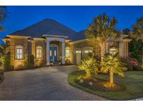 Elegant brick home with a circular driveway, lush landscaping, and a well-lit exterior at twilight at 1108 Surf Pointe Dr., North Myrtle Beach, SC 29582