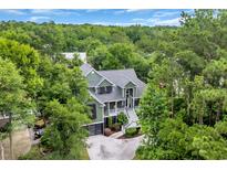 Aerial view of a two-story home nestled amongst lush trees with a private driveway and manicured lawn at 24 Jerry Ct., Pawleys Island, SC 29585