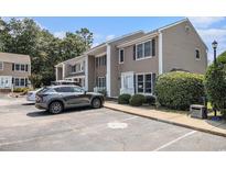 Tan townhouse with black shutters and a parking area in front of the building surrounded by mature trees and blue skies at 6702 Jefferson Pl. # C6, Myrtle Beach, SC 29572