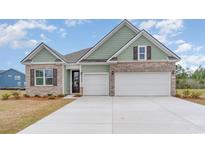 Charming home featuring a two-car garage, brick accents, and light green siding beneath a blue sky at 7175 Shooting Star Way, Myrtle Beach, SC 29579