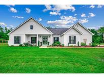 Charming home boasts a bright green lawn, black shutters, and a covered porch entry with rocking chairs at 101 Karlie Ln., Aynor, SC 29511