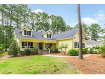 Charming yellow home featuring a welcoming front porch, black shutters, and lush green landscaping at 786 Wild Oak Ln. Nw, Calabash, NC 28467