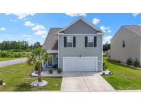 Charming two-story home featuring light gray siding, a two-car garage, and a neatly landscaped front yard with a small palm tree at 798 Woodland Farms Circle, Aynor, SC 29511