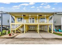 Charming yellow stilted beach house with a covered parking area and a cozy balcony with ceiling fans at 121 Easy St., Garden City Beach, SC 29576