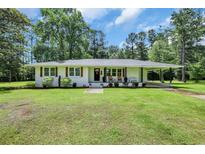 Charming single-story white brick home featuring a well-manicured lawn and cozy front porch with rocking chairs at 265 Powell Loop, Andrews, SC 29510