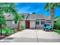 Charming home featuring a vibrant red door, palm trees, manicured landscaping, and a golf cart parked in the driveway at 10056 Kings Rd., Myrtle Beach, SC 29572