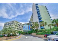Exterior of the Coral Beach Resort featuring a parking area, palm trees, and blue accents against a cloudy sky at 1105 S Ocean Blvd. # 330, Myrtle Beach, SC 29577