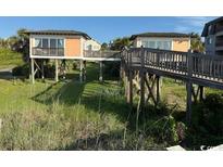 Coastal homes connected by a wooden walkway, surrounded by lush greenery and glimpses of sandy dunes at 5732 N Ocean Blvd., Myrtle Beach, SC 29577