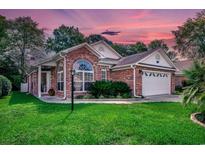 Charming brick home featuring manicured lawn and garden beds under a colorful evening sky at 1010 Swan Lake Dr., North Myrtle Beach, SC 29582