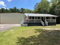 Charming home with a covered porch, American flag, metal roof, and a large metal outbuilding at 2879 Waccamaw Cove, Longs, SC 29568