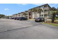 Exterior view of condo building with ample parking and tropical landscaping on a bright sunny day at 5601 N Ocean Blvd. # E-113, Myrtle Beach, SC 29577