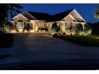 Charming brick home at night featuring landscape lighting, mature shrubs, and large driveway at 1009 Maccoa Dr., Conway, SC 29526