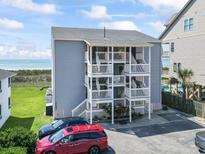 Three story condo building with white railings and stairs with a parking lot and partial ocean view at 4105 S Ocean Blvd. # 102, North Myrtle Beach, SC 29582