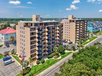 Condo building with a beige facade, balconies, green lawn, mature trees, and parking spaces on a sunny day at 7601 N Ocean Blvd. # 3-B, Myrtle Beach, SC 29572